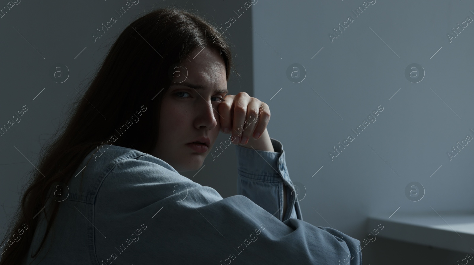 Photo of Sad young woman crying near grey wall indoors, space for text