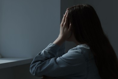 Photo of Sad young woman crying near grey wall indoors