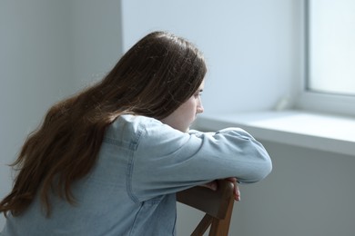 Photo of Sad young woman near window at home
