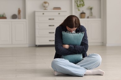 Photo of Sad young woman with pillow sitting on floor at home, space for text
