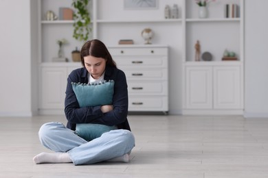 Photo of Sad young woman with pillow sitting on floor at home, space for text