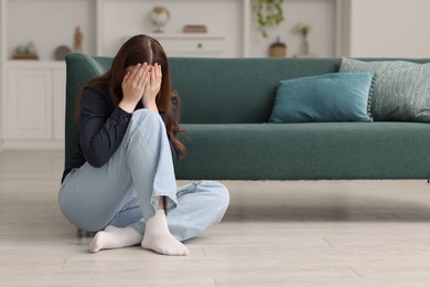 Photo of Sad young woman crying on floor at home, space for text