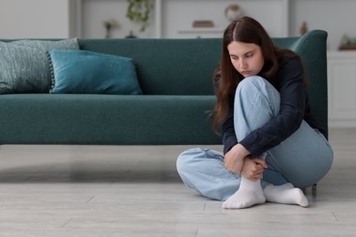 Photo of Sad young woman sitting on floor at home, space for text