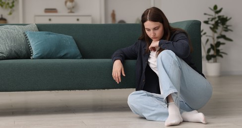 Photo of Sad young woman sitting on floor at home, space for text