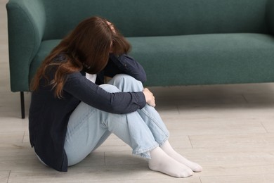 Photo of Sad young woman crying on floor at home, space for text