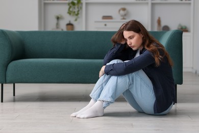 Photo of Sad young woman sitting on floor at home, space for text