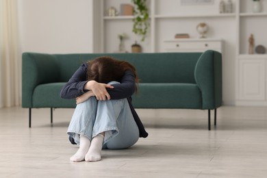 Photo of Sad young woman crying on floor at home, space for text