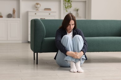 Photo of Sad young woman sitting on floor at home