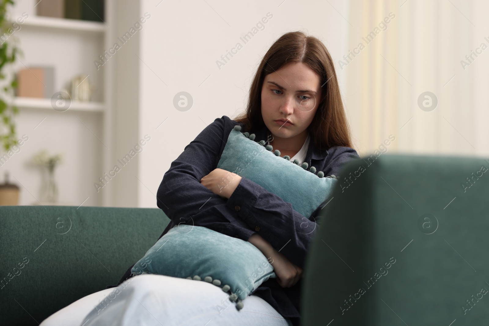 Sad young woman with pillow sitting on sofa at home Photo of Sad young woman with pillow sitting on sofa at home