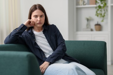 Photo of Sad young woman sitting on sofa at home, space for text