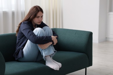 Photo of Sad young woman sitting on sofa at home, space for text
