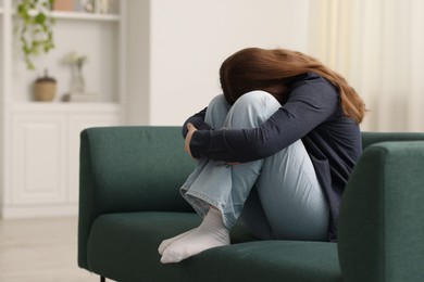 Photo of Sad young woman crying on sofa at home, space for text
