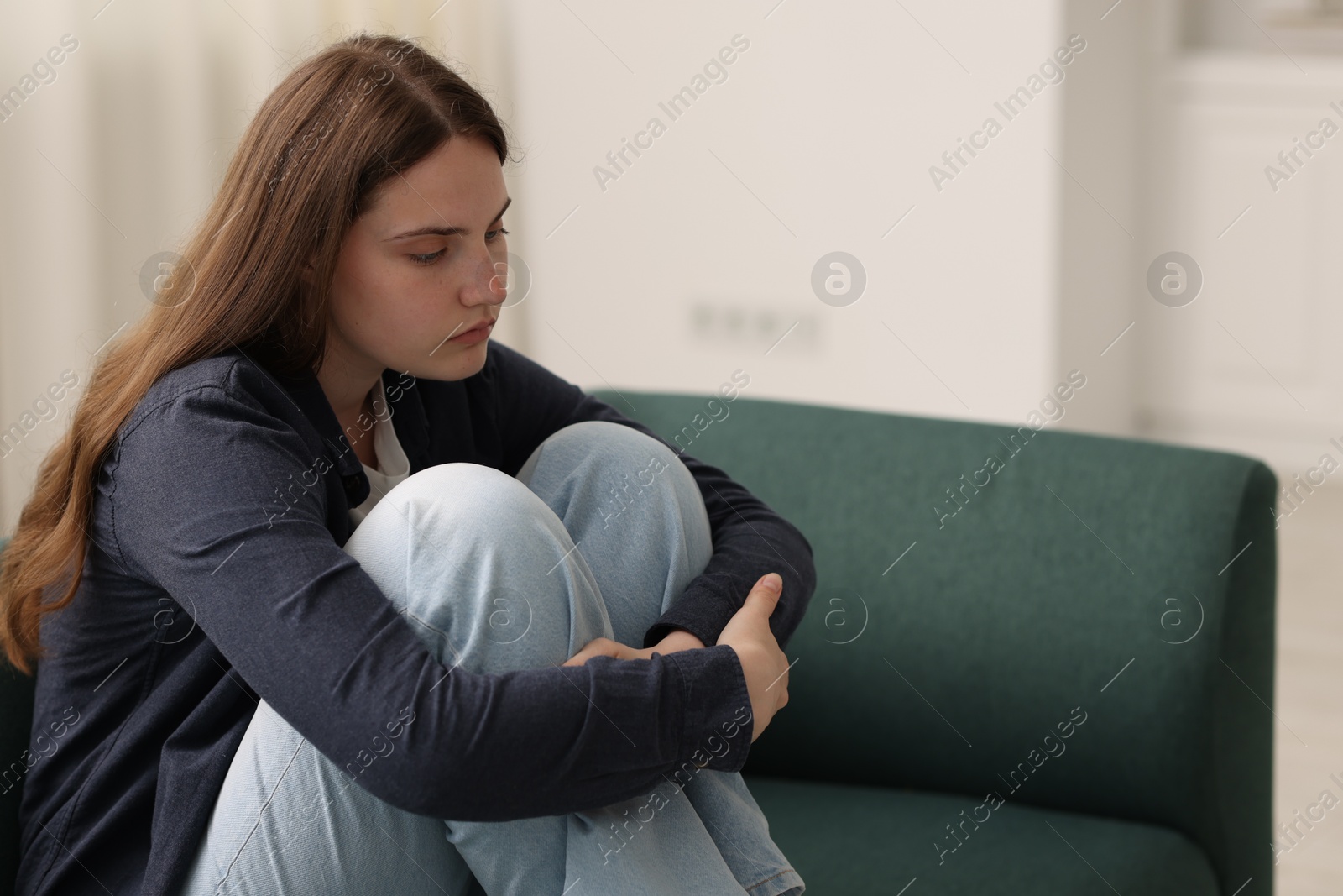 Sad young woman sitting on sofa at home, space for text Photo of Sad young woman sitting on sofa at home, space for text