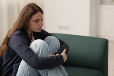 Photo of Sad young woman sitting on sofa at home, space for text