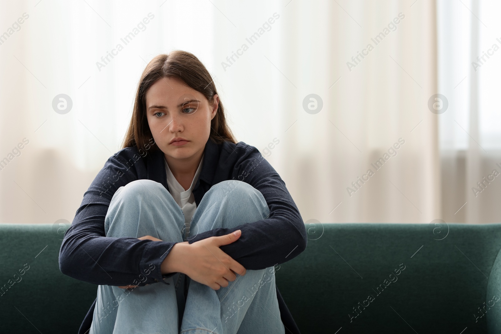 Sad young woman sitting on sofa at home, space for text Photo of Sad young woman sitting on sofa at home, space for text