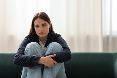 Photo of Sad young woman sitting on sofa at home, space for text