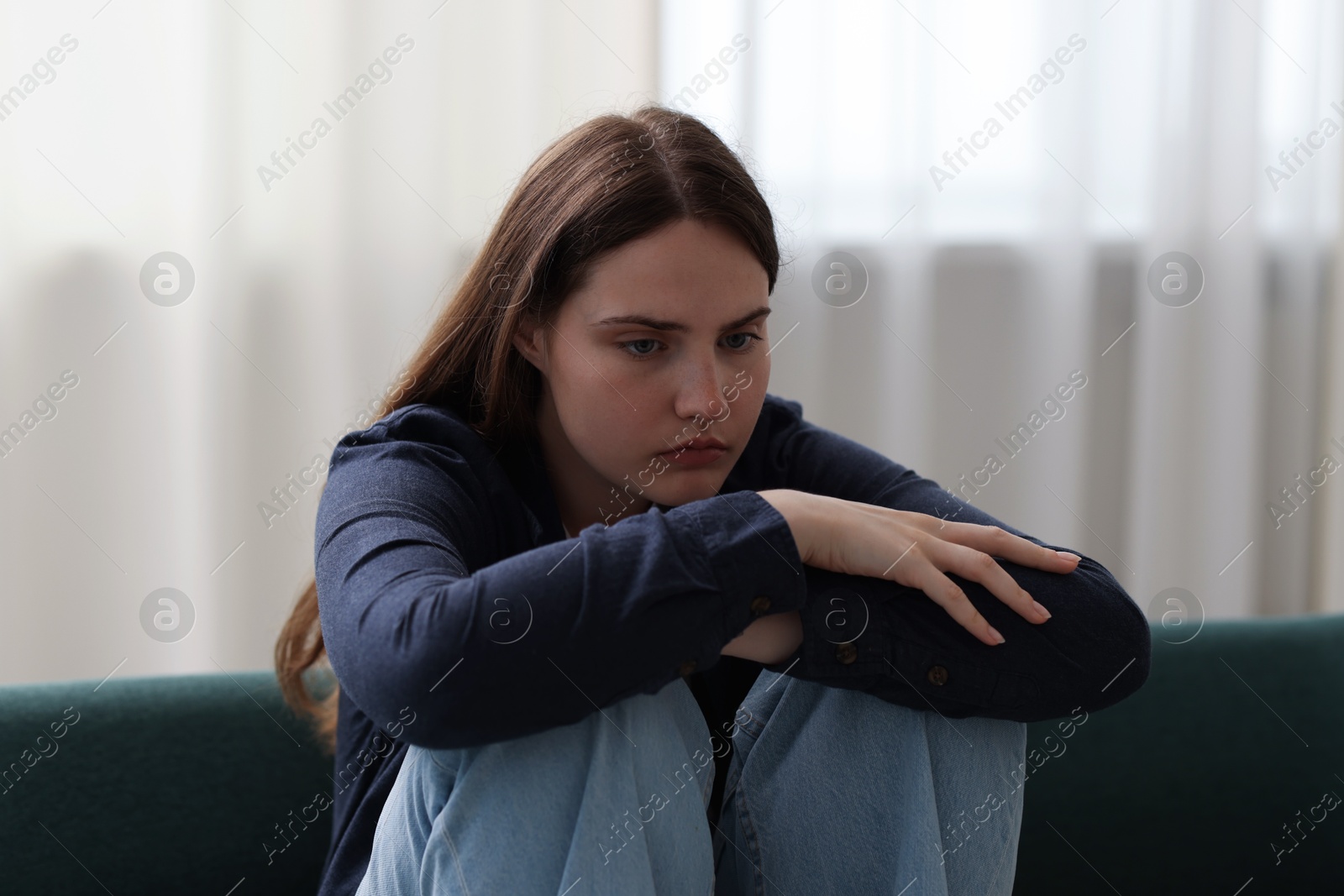 Sad young woman sitting on sofa at home Photo of Sad young woman sitting on sofa at home