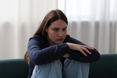 Photo of Sad young woman sitting on sofa at home