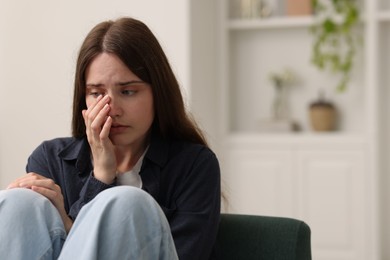 Photo of Sad young woman sitting on sofa at home, space for text