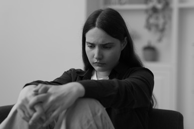 Photo of Sad young woman sitting on sofa at home. Black and white effect