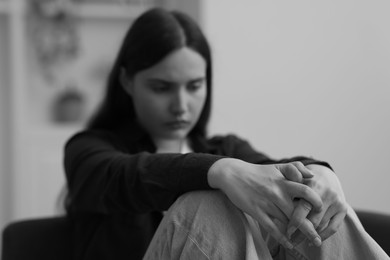 Photo of Sad young woman sitting on sofa at home. Black and white effect