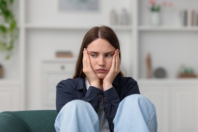 Photo of Sad young woman sitting on sofa at home