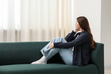 Photo of Sad young woman sitting on sofa at home, space for text