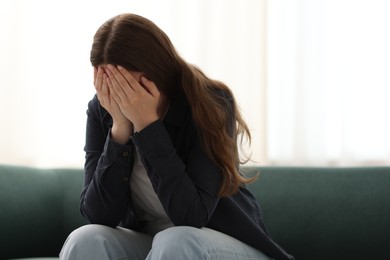 Photo of Sad young woman crying on sofa at home, space for text