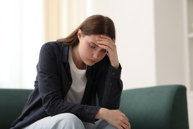 Photo of Sad young woman sitting on sofa at home