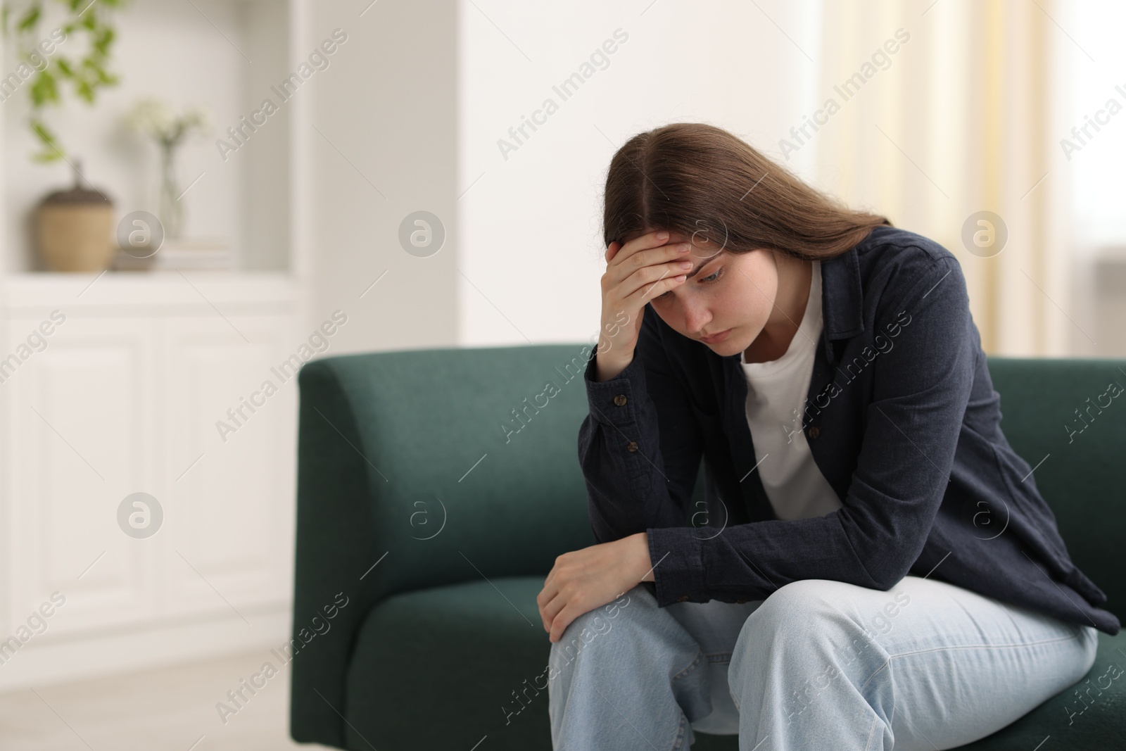 Sad young woman sitting on sofa at home, space for text Photo of Sad young woman sitting on sofa at home, space for text