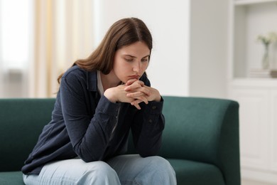 Photo of Sad young woman sitting on sofa at home, space for text