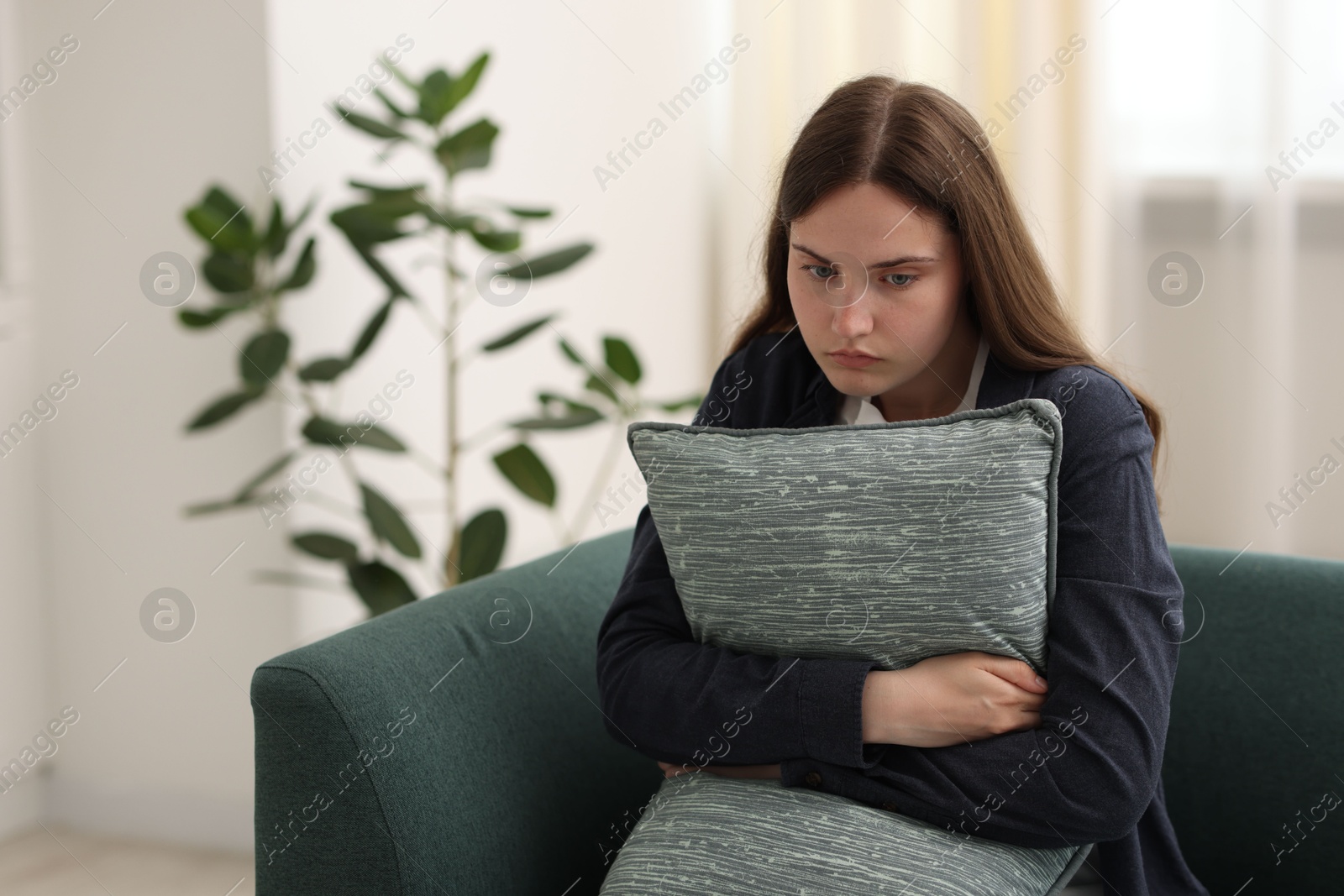 Photo of Sad young woman with pillow sitting on sofa at home, space for text