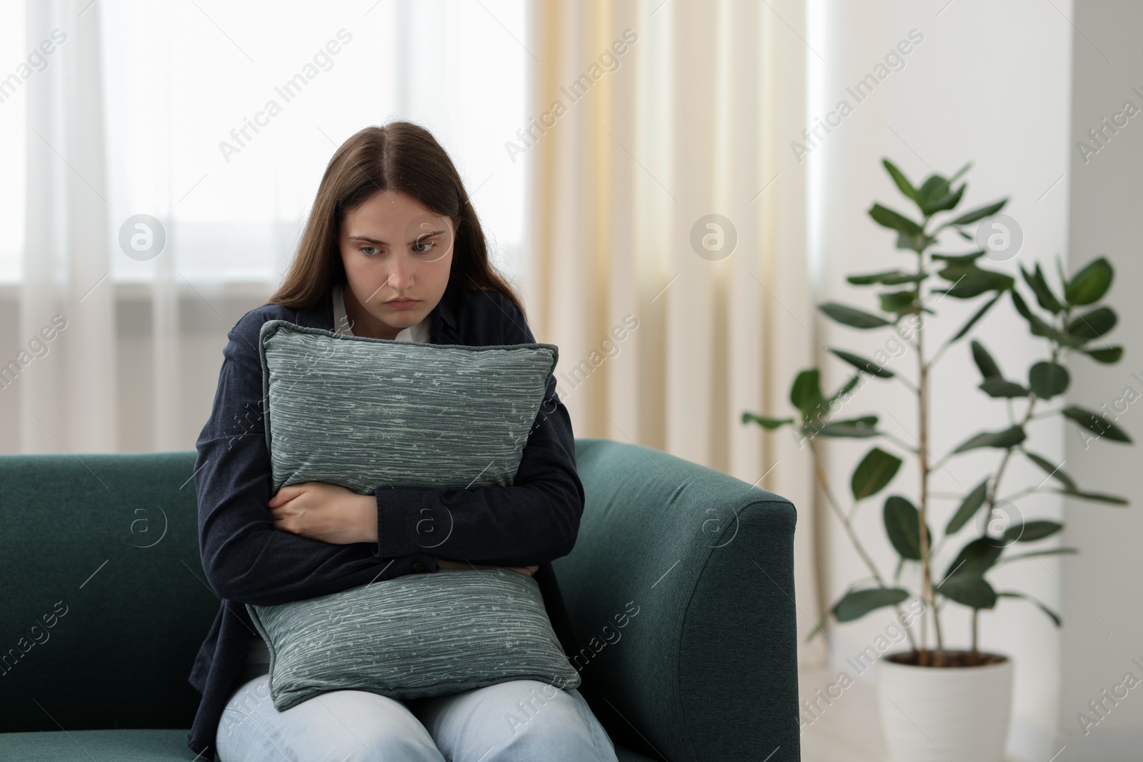 Sad young woman with pillow sitting on sofa at home, space for text Photo of Sad young woman with pillow sitting on sofa at home, space for text