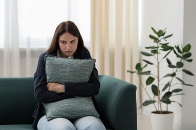 Photo of Sad young woman with pillow sitting on sofa at home, space for text