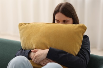 Photo of Sad young woman with pillow sitting on sofa at home