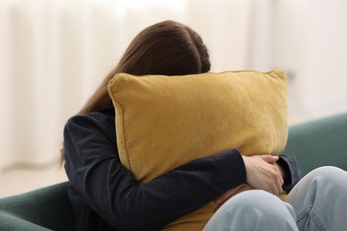 Photo of Sad young woman with pillow sitting on sofa at home