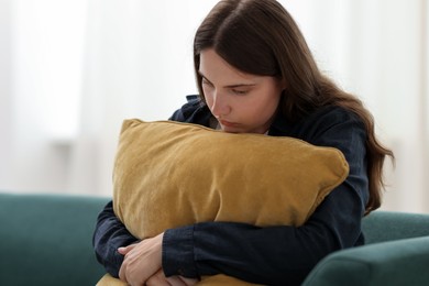 Photo of Sad young woman with pillow sitting on sofa at home