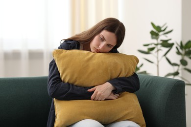 Photo of Sad young woman with pillow sitting on sofa at home