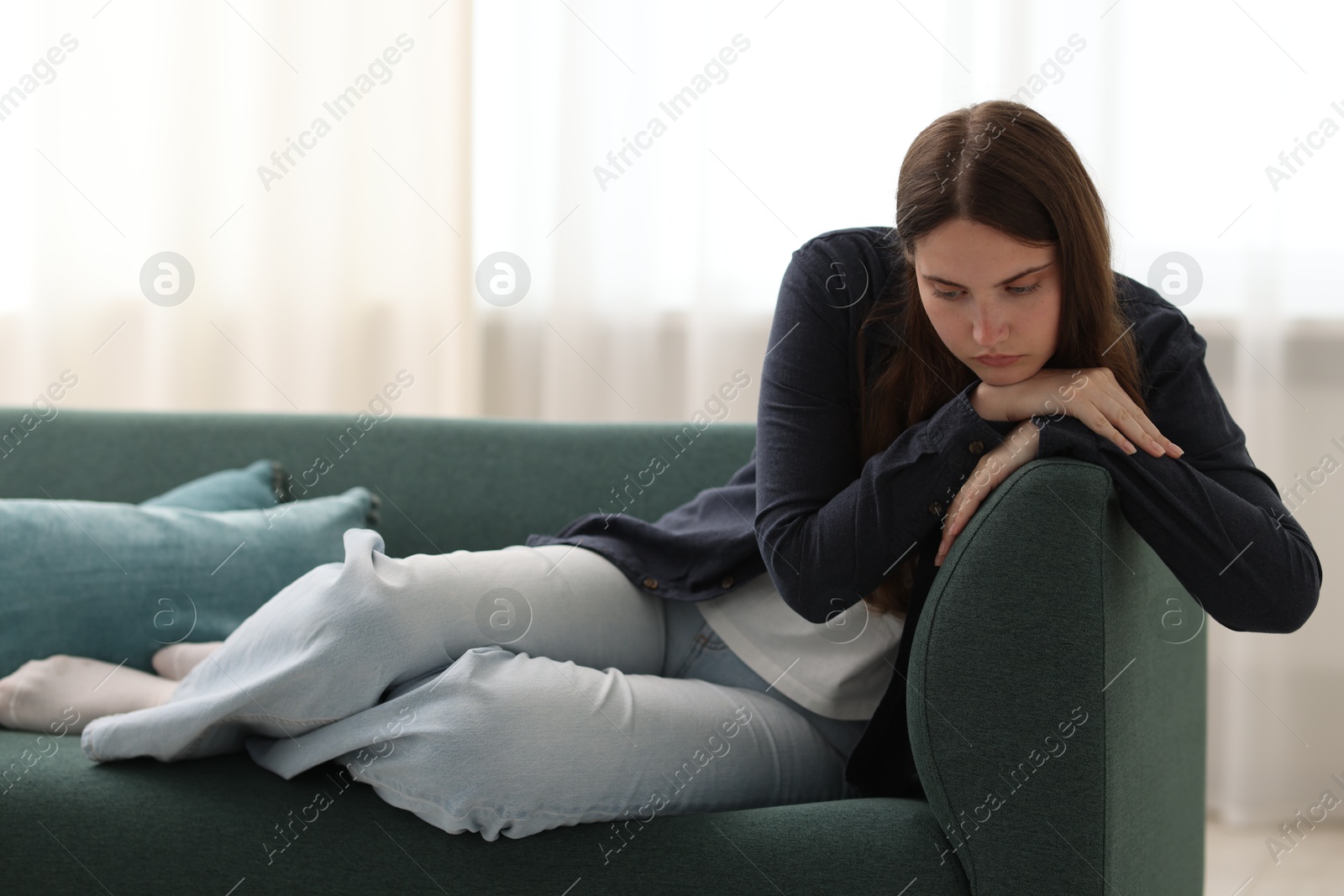 Photo of Sad young woman sitting on sofa at home