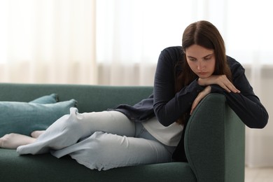 Photo of Sad young woman sitting on sofa at home