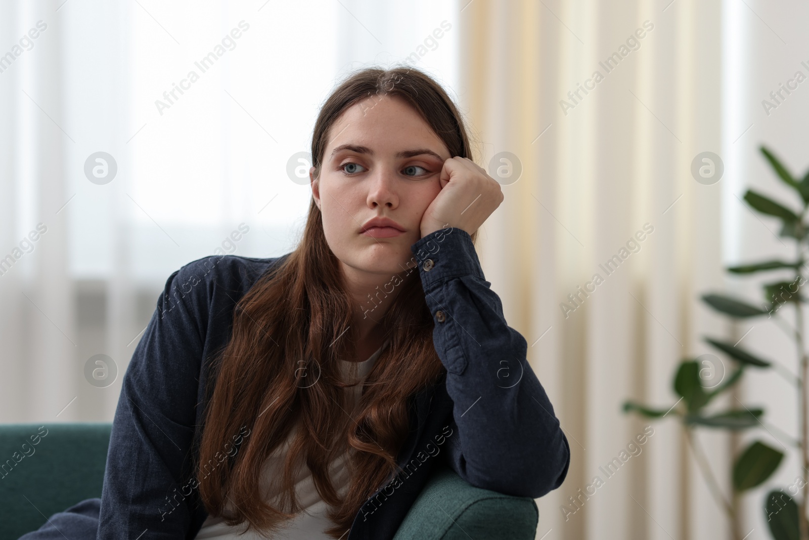Photo of Sad young woman sitting on sofa at home, space for text