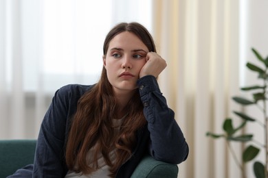 Photo of Sad young woman sitting on sofa at home, space for text