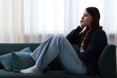 Photo of Sad young woman sitting on sofa at home