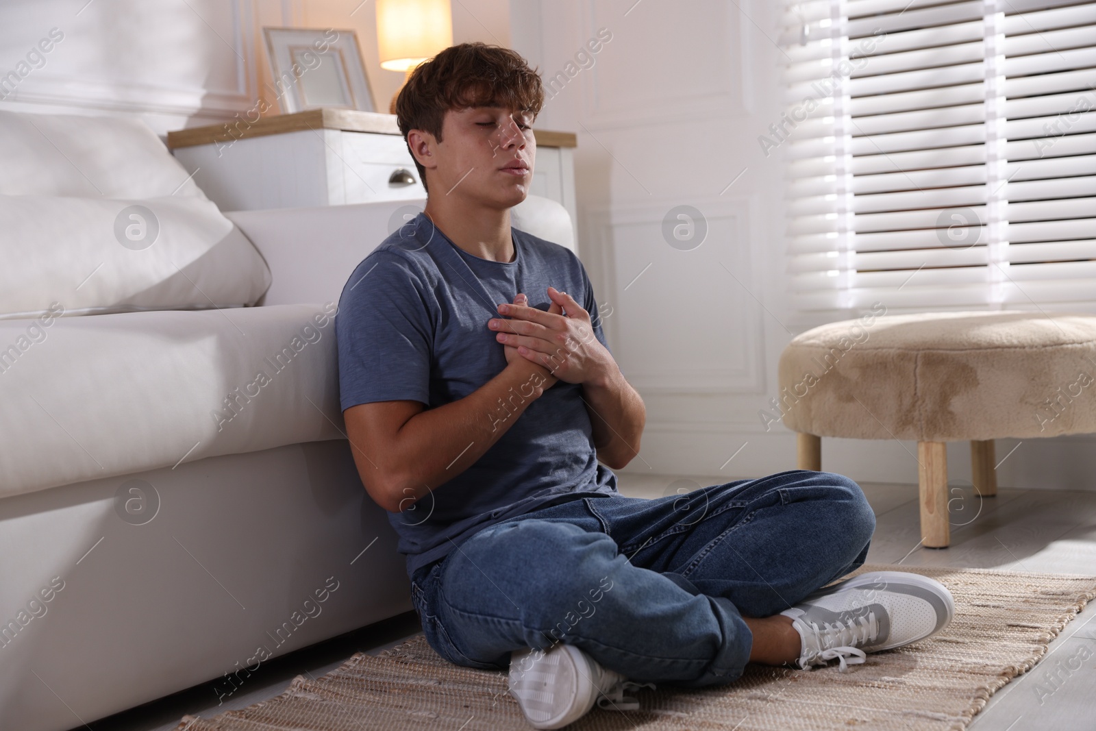 Photo of Teenage boy meditating near sofa at home. Way to stop panic attack