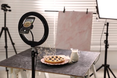 Photo of Shooting tasty pie and milk with smartphone in studio, selective focus. Professional food photography