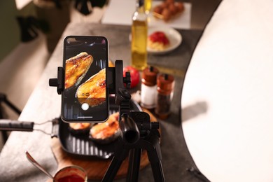 Photo of Shooting tasty roasted fish with smartphone in studio, selective focus. Professional food photography