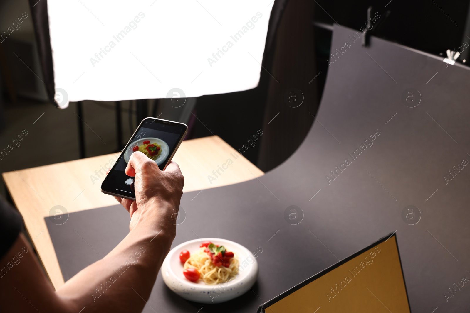 Photo of Man taking picture of pasta with smartphone in studio, closeup. Professional food photography