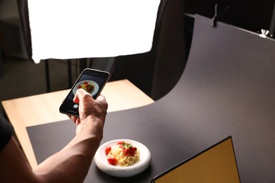 Photo of Man taking picture of pasta with smartphone in studio, closeup. Professional food photography