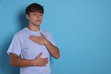 Photo of Teenage boy deep breathing on light blue background, space for text. Way to stop panic attack