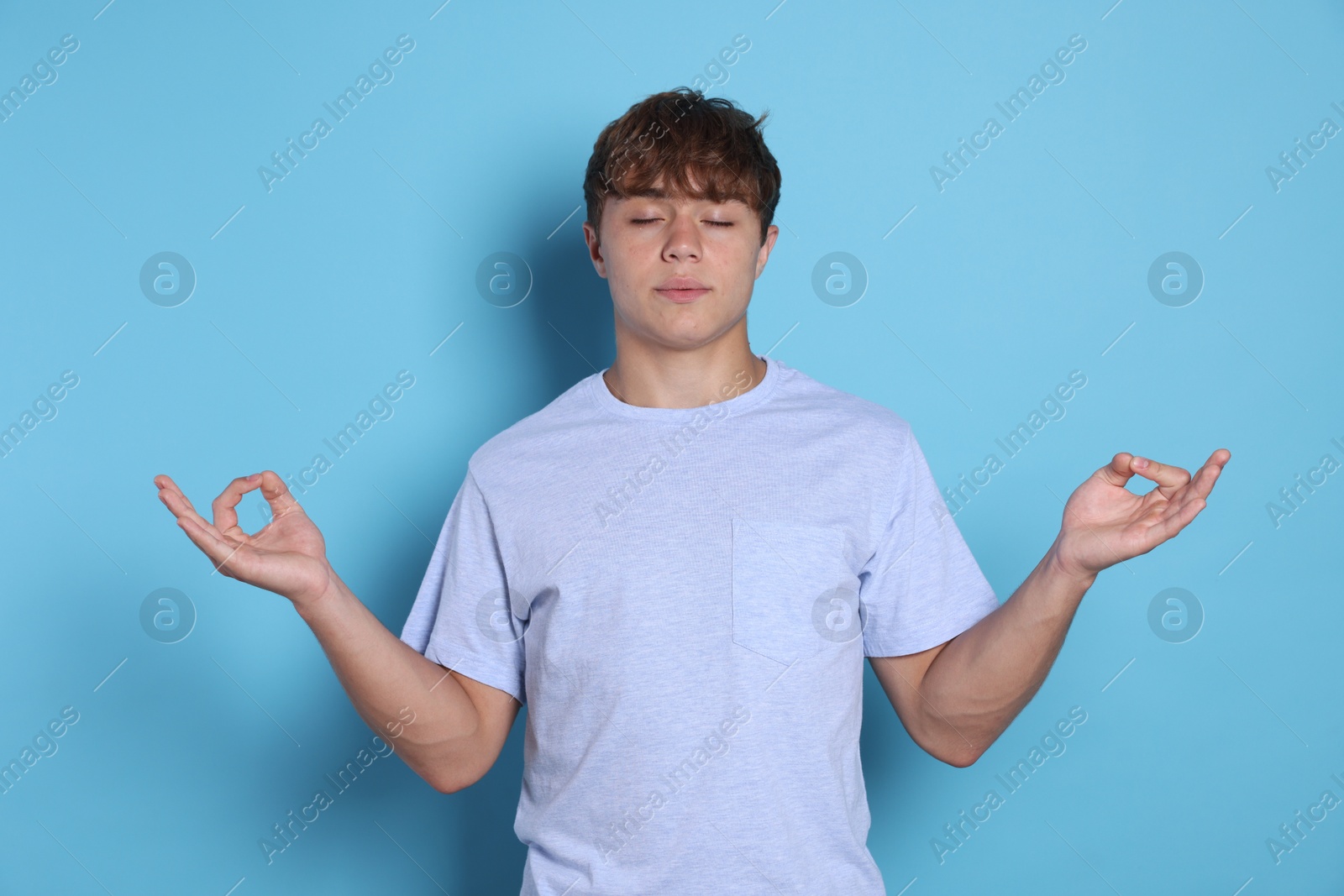 Photo of Teenage boy meditating on light blue background. Way to stop panic attack